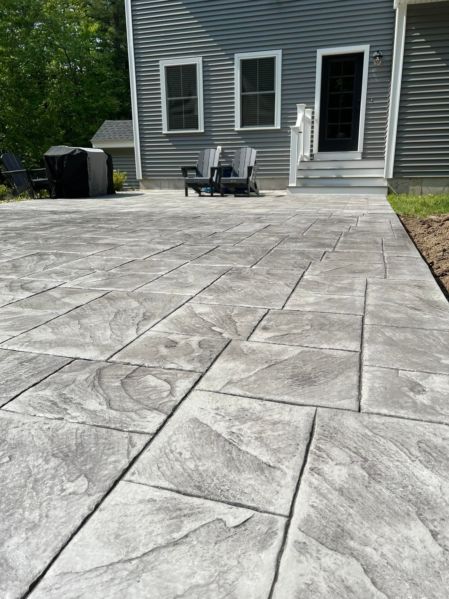 A patio with chairs and a grill in front of a house.