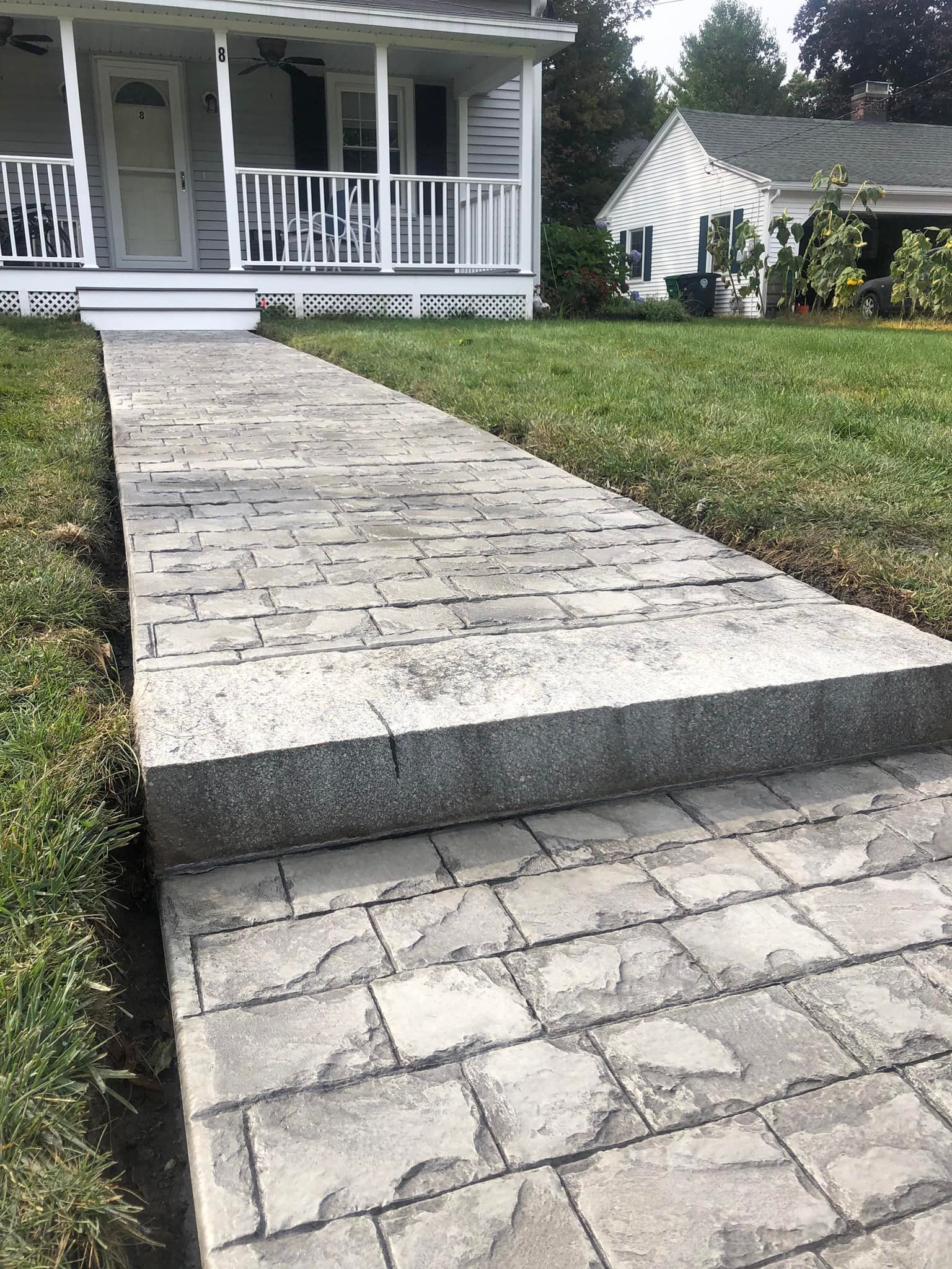 A concrete walkway leading to a house with a porch.