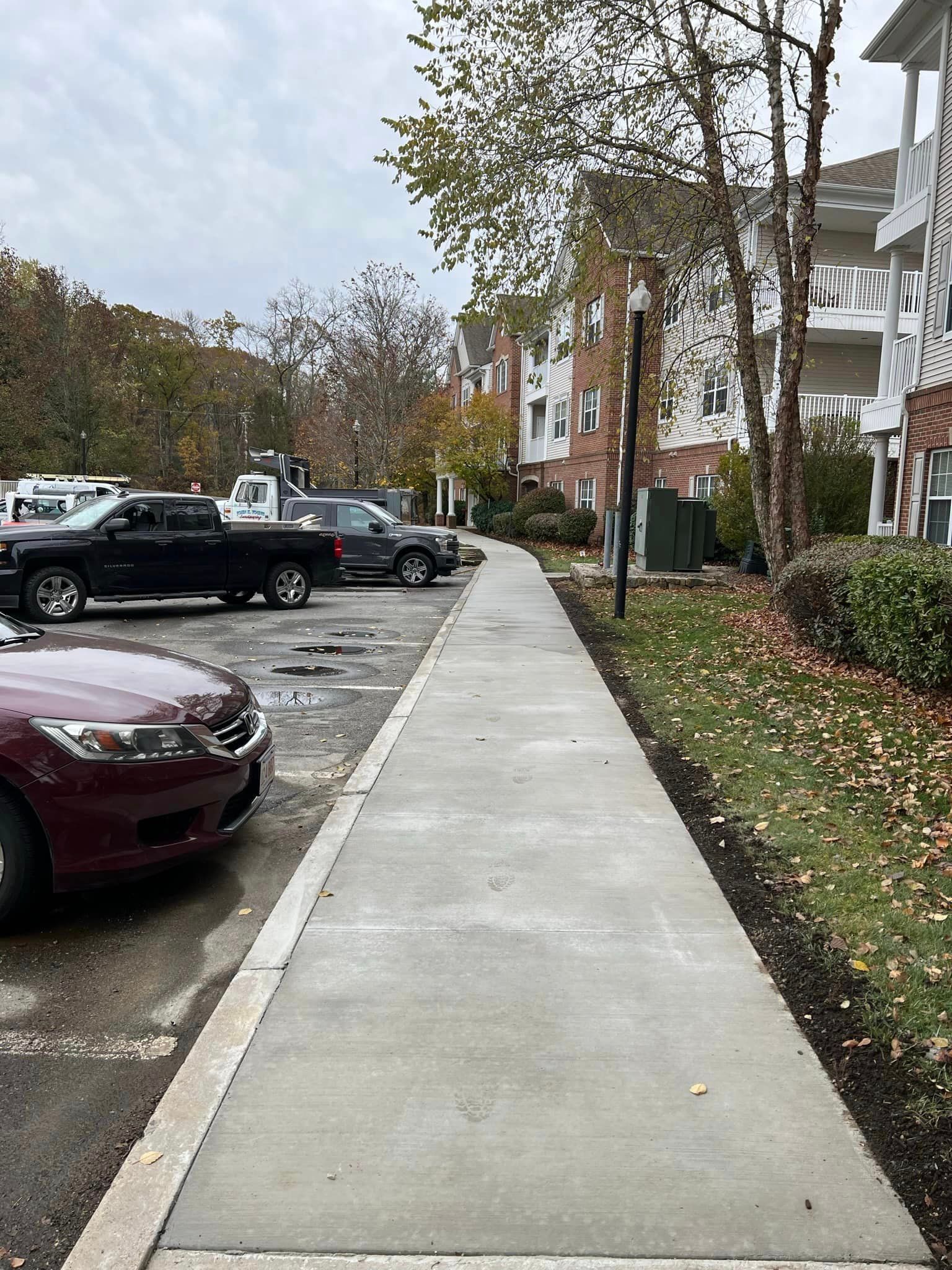 A red car is parked on a sidewalk next to a parking lot.