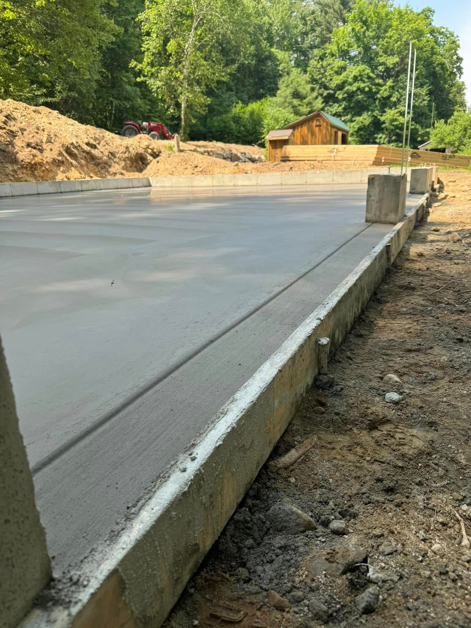 A concrete driveway with a wooden shed in the background is being built.