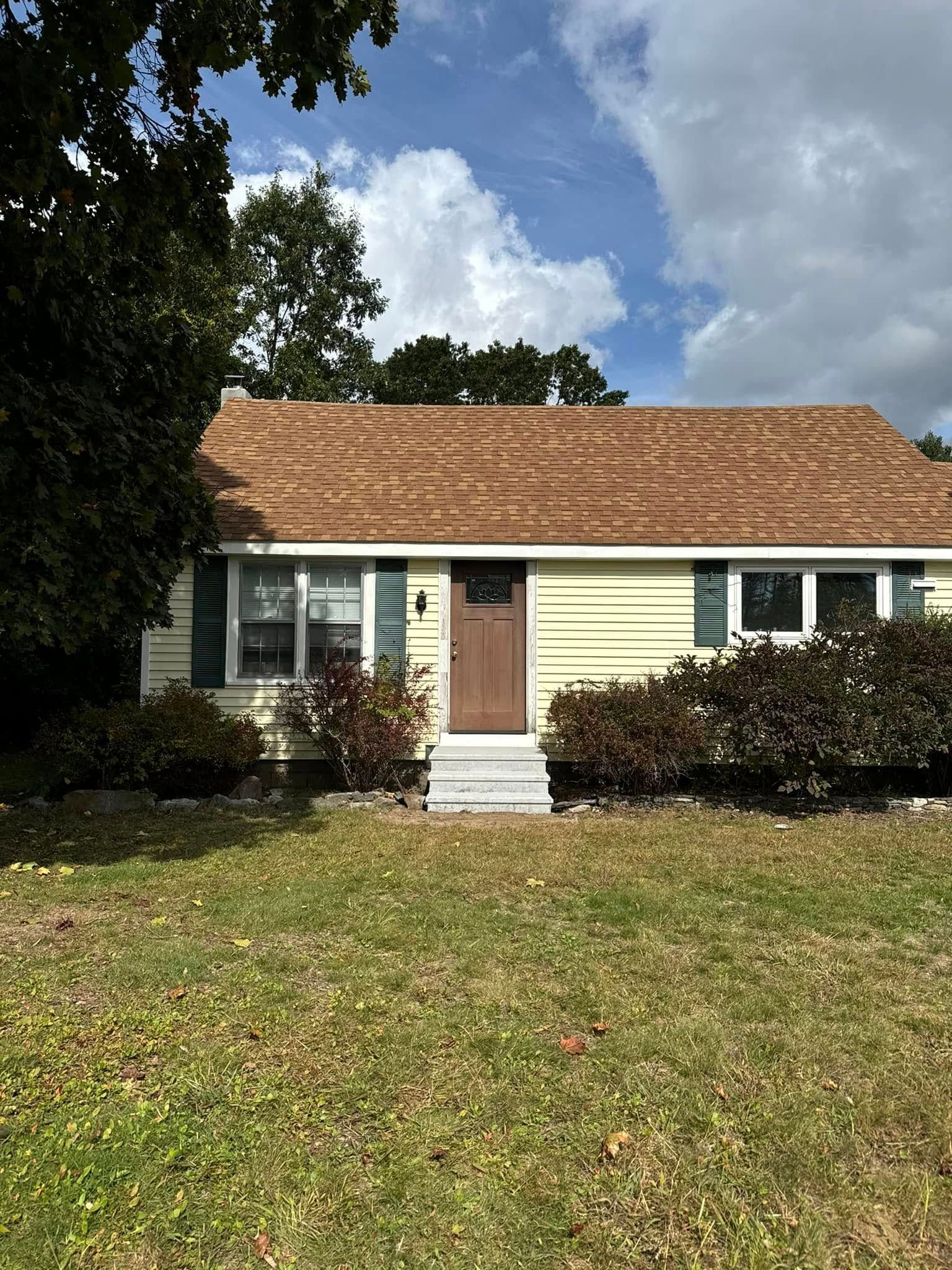 A yellow house with a brown roof and green shutters