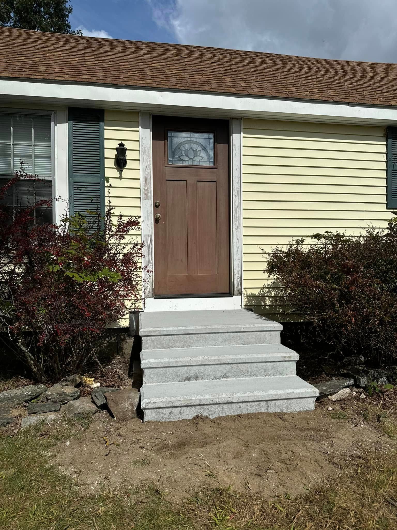 A yellow house with a brown door and concrete steps