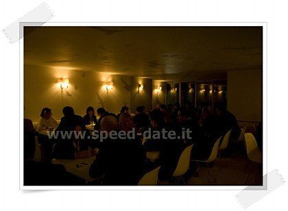 Un gruppo di persone è seduto ai tavoli in una stanza buia e il sito è www.speed-date.it