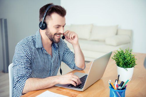 Un uomo che indossa le cuffie è seduto alla scrivania e utilizza un computer portatile per fare speed dating online