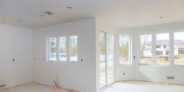 Electrician in yellow hard hat and overalls working on electrical panel near a window.
