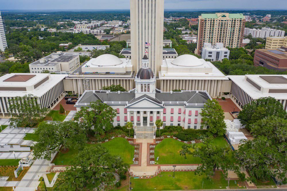 Aerial view of a large government building in Tallahassee with a tall central tower, white façade, and green lawns.