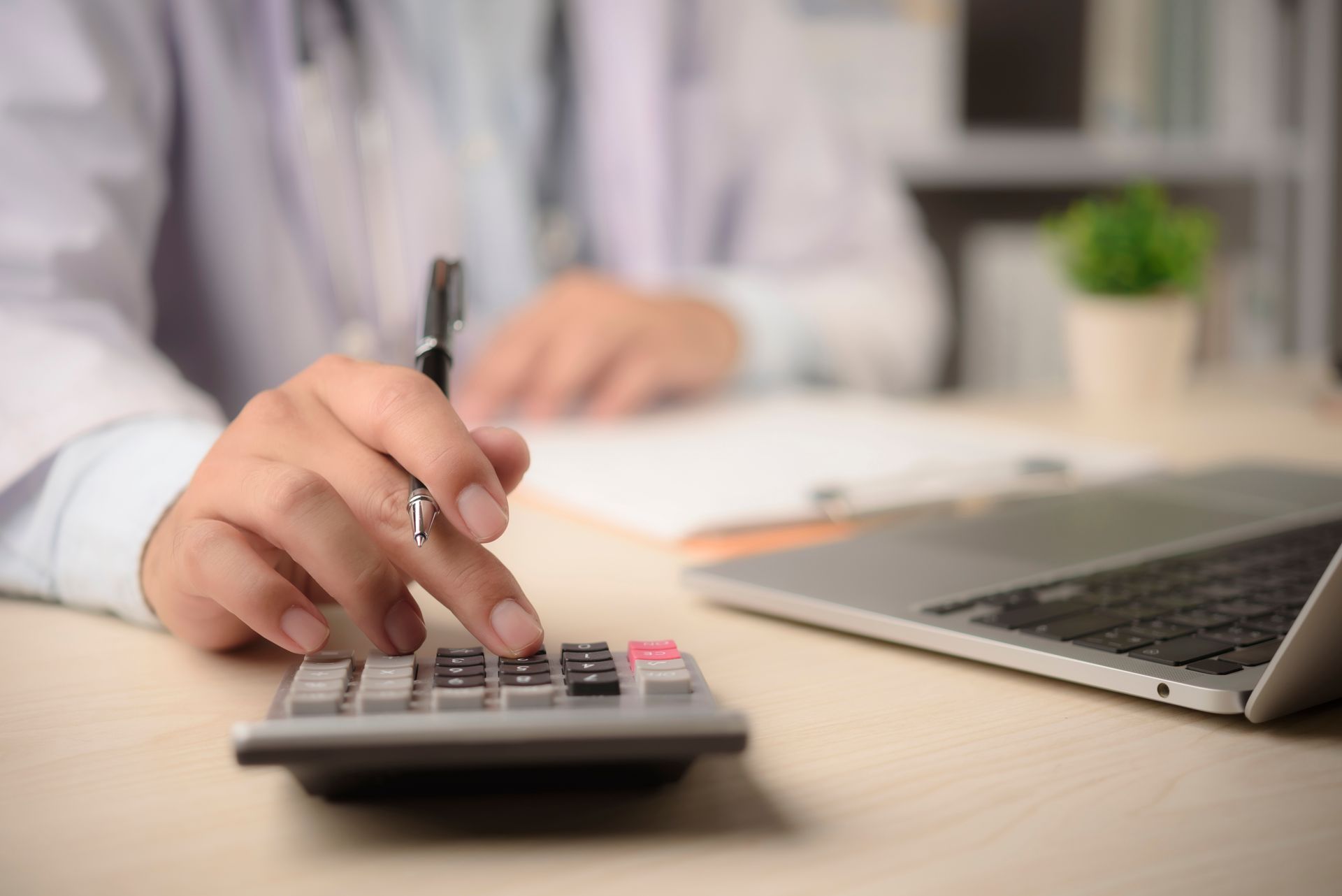 Hand using calculator next to laptop on desk in an office setting calculating the cost of Legal malpractice insurance