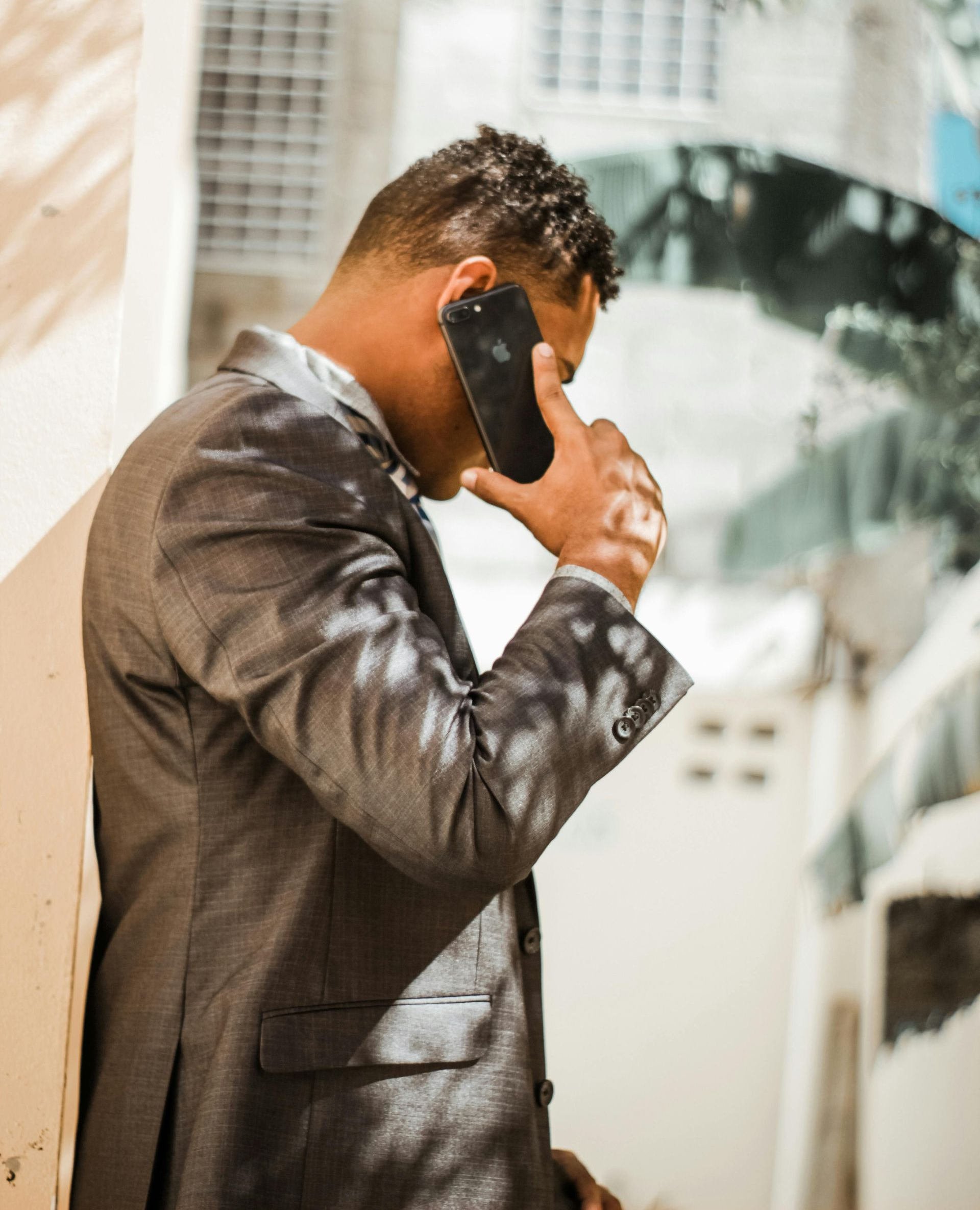 Man in a gray suit speaking on a phone in a bright city setting