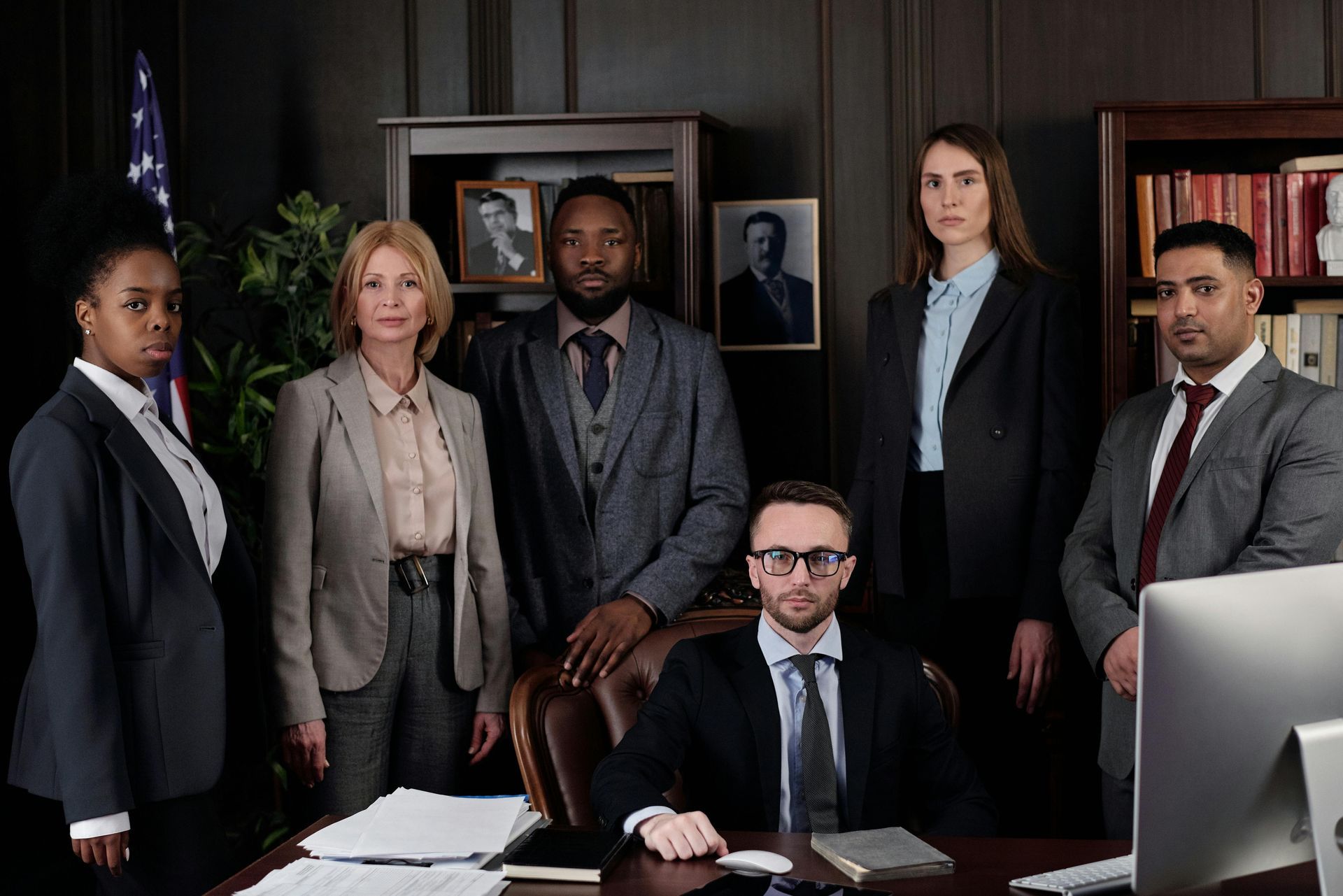 Five professionals posing in a wood-paneled office, with a man seated at a desk in front.