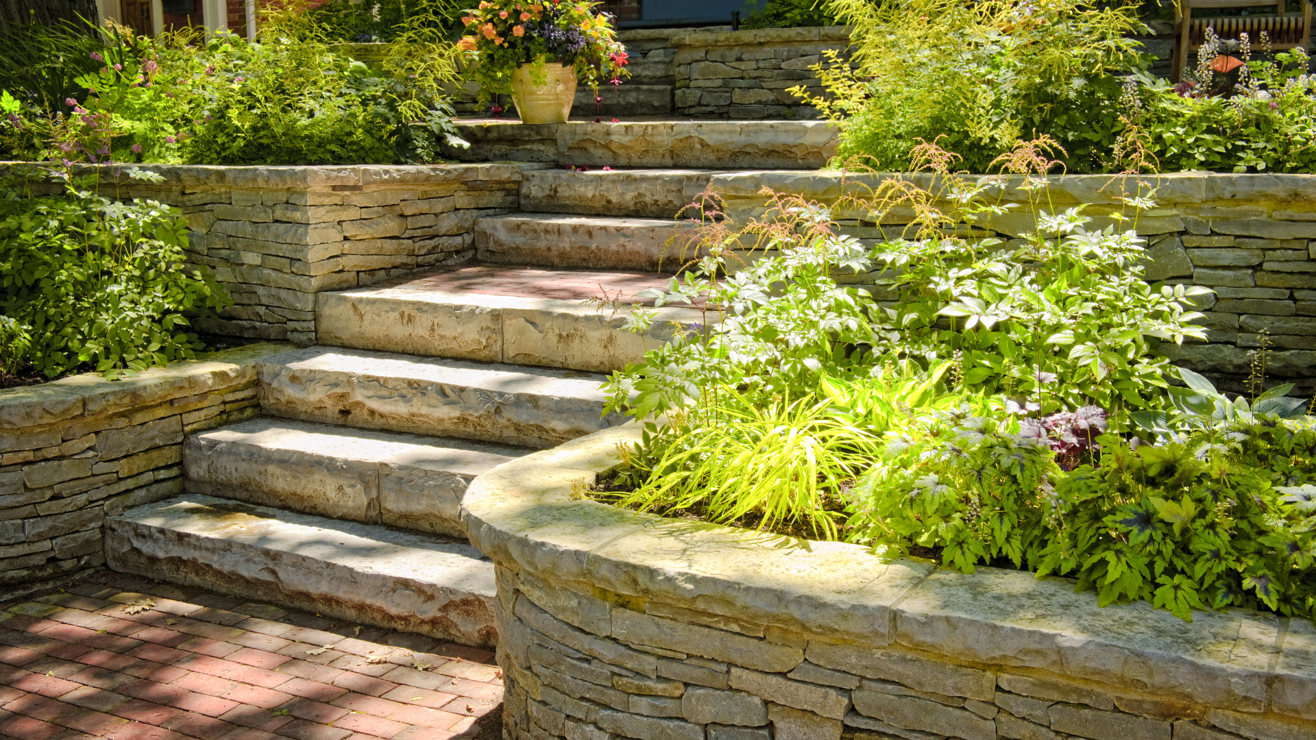 A stone wall surrounds a set of stairs in a garden.