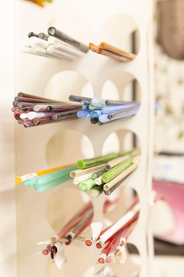 Kleurrijke glazen staven tentoongesteld in een wit rek. Verschillende tinten rood, blauw, groen en bruin zijn zichtbaar.