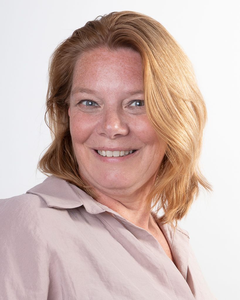 Vrouw met rood haar en een glimlach, gekleed in een beige shirt, tegen een witte achtergrond.