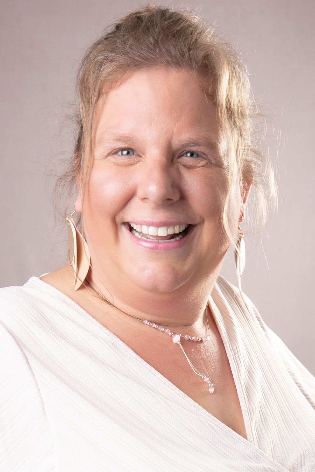 Lachende vrouw met een lichte huid, gekleed in een wit topje en sieraden.