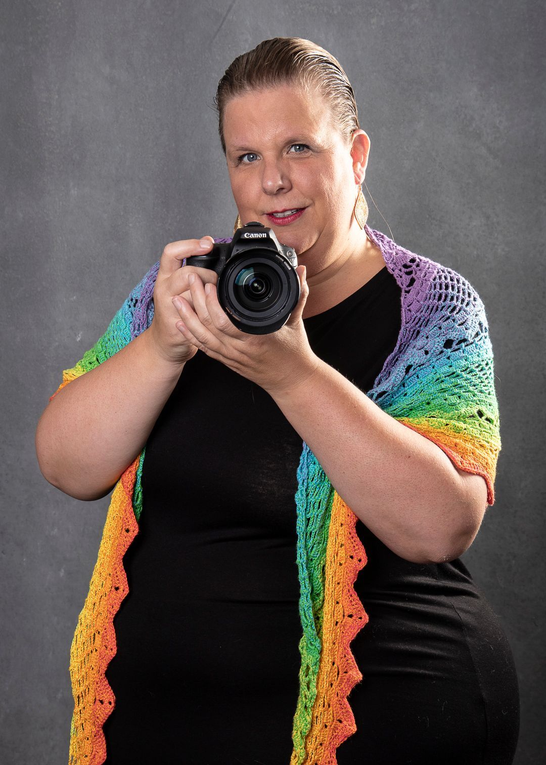 Vrouw met camera, gekleed in een regenboogsjaal. Studiofoto tegen een grijze achtergrond.