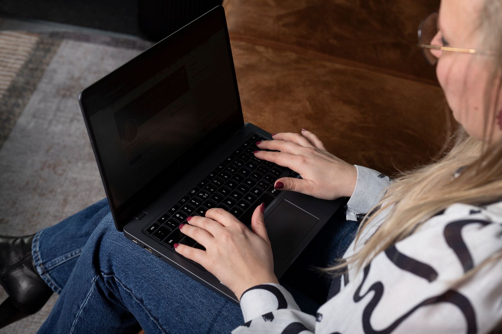 Een persoon die op een laptop typt terwijl hij op een bruine bank zit.