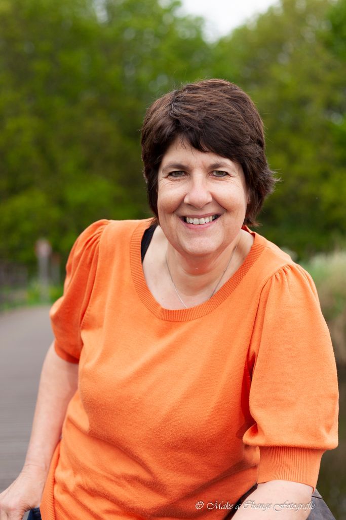 Een vrouw in een oranje shirt lacht naar de camera.