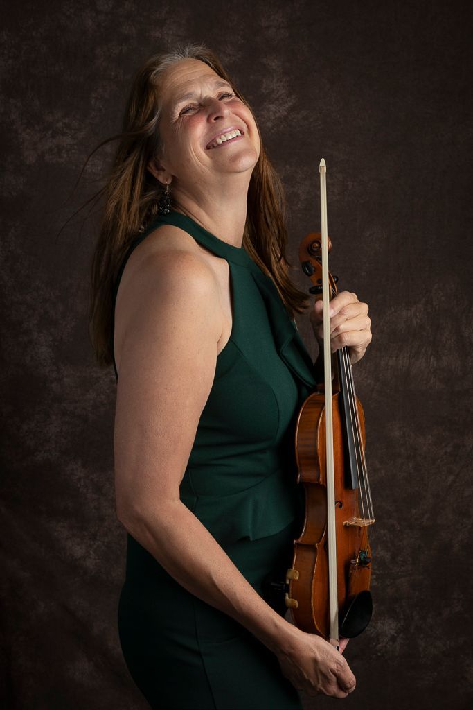 Een vrouw in een groene jurk houdt een viool vast en lacht.