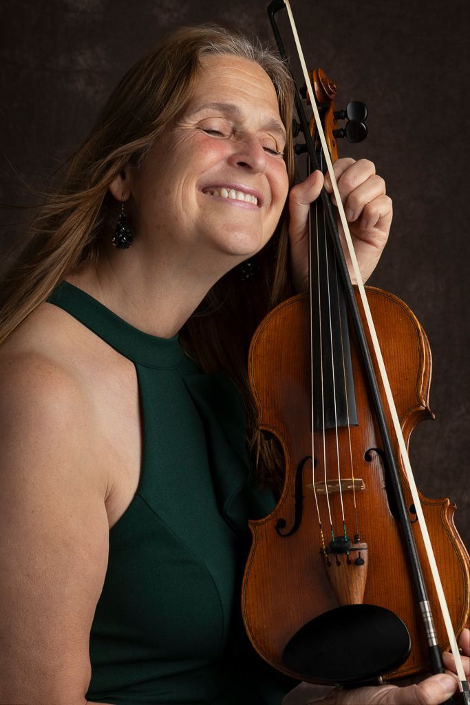 Een vrouw in een groen tanktopje lacht terwijl ze een viool vasthoudt.