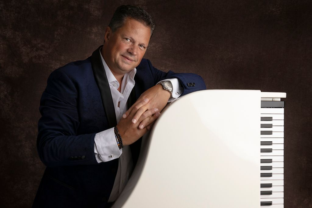 Een man in pak leunt tegen een witte piano.