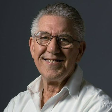 Een man met een bril en een wit overhemd zit met zijn armen over elkaar.