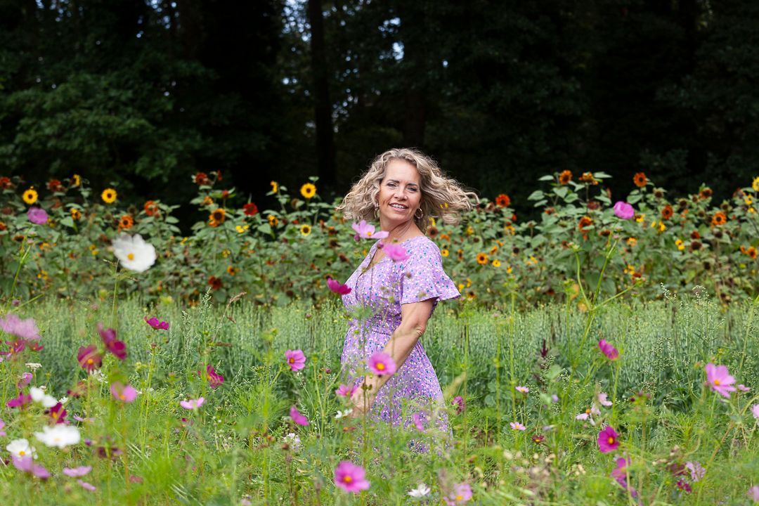 Een vrouw in een paarse jurk staat in een bloemenveld.