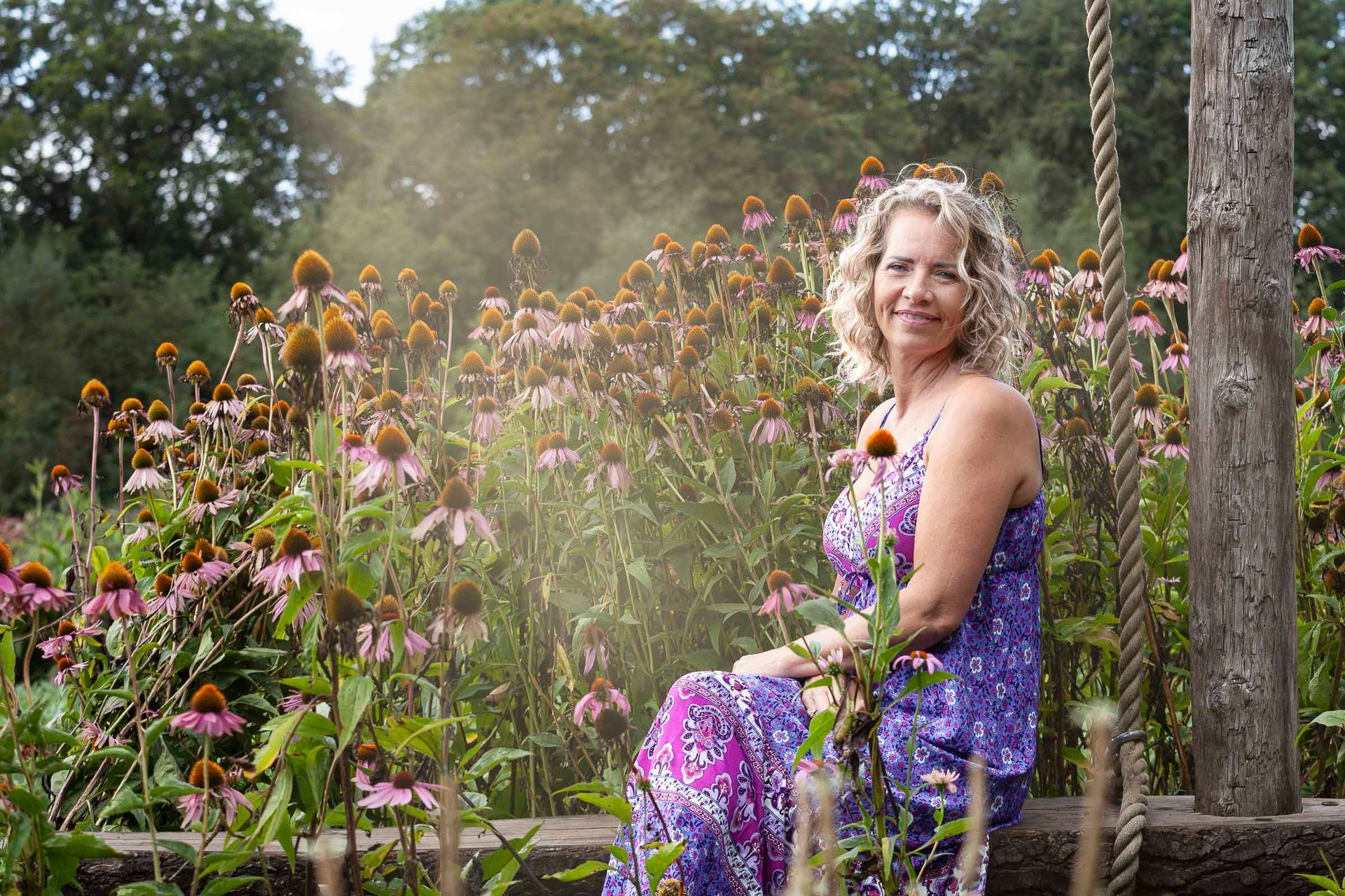 Een vrouw in een paarse jurk zit op een schommel in een tuin.