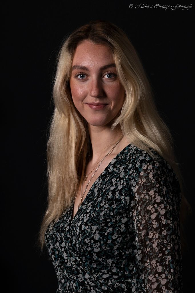 Een vrouw met lang blond haar draagt ​​een shirt met bloemen en een ketting.