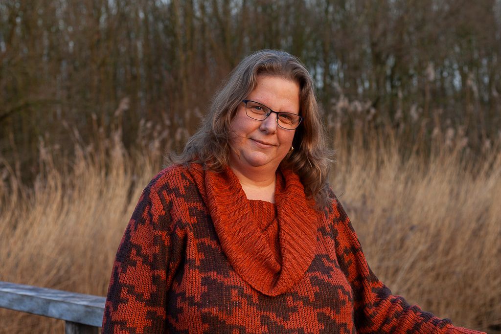 Foto van Karin van Es, fotograaf en eigenaar van Make a Change Fotografie in een natuurlijke omgeving tijdens het gouden uur met een oranje met bruine trui aan.