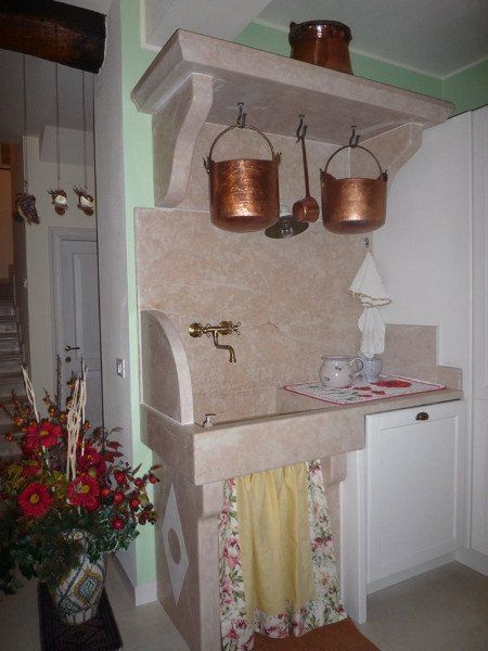 Rincon di una cucina dove un pezzo di marmo che comprende una ripiano,il rivestimento di pareti e il lavabo sono in marmo. Vecchi utensili di rame decorano lo spazio