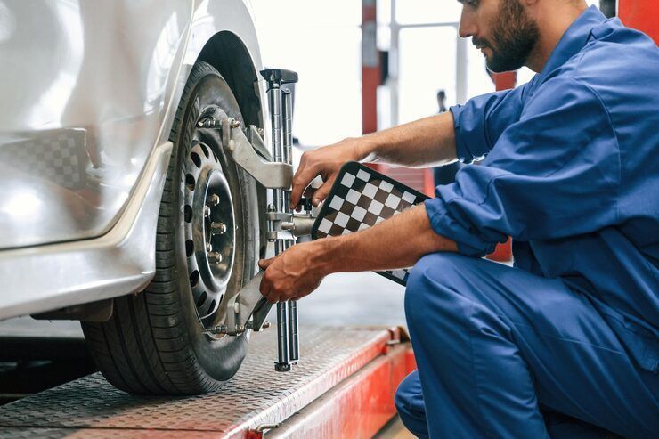 Mechanic adjusting car wheel alignment with a checkerboard-like tool in a repair shop.