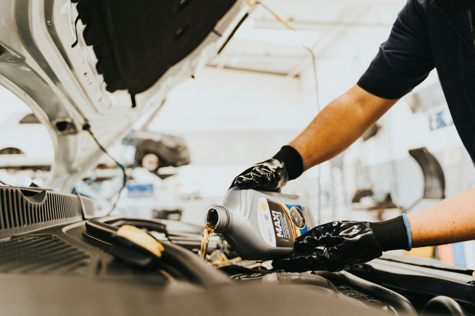 Mechanic pouring oil into a car engine with the hood open in a garage.