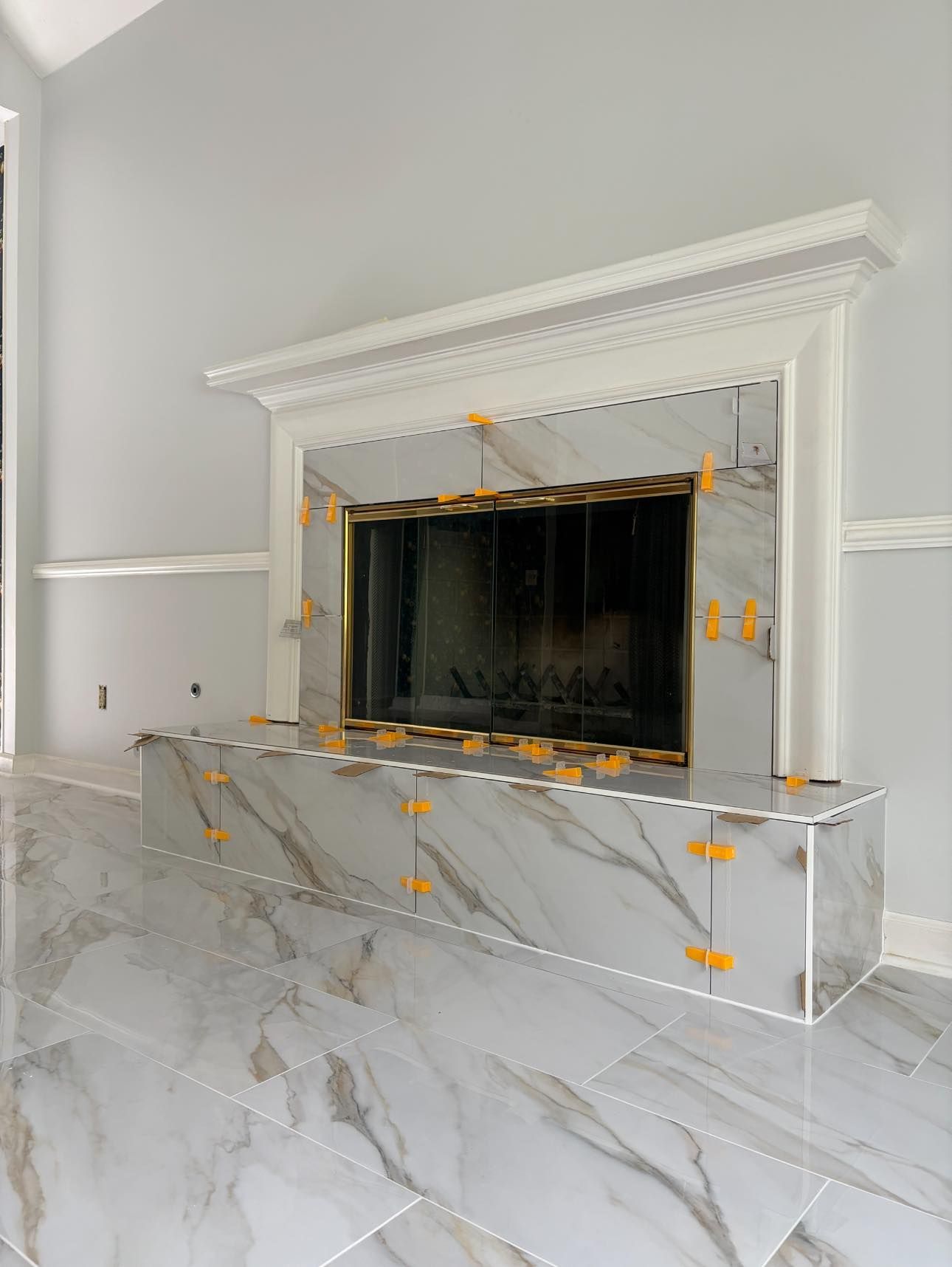Fireplace surround under construction, featuring gray marble-look tiles. Orange tile spacers are visible.
