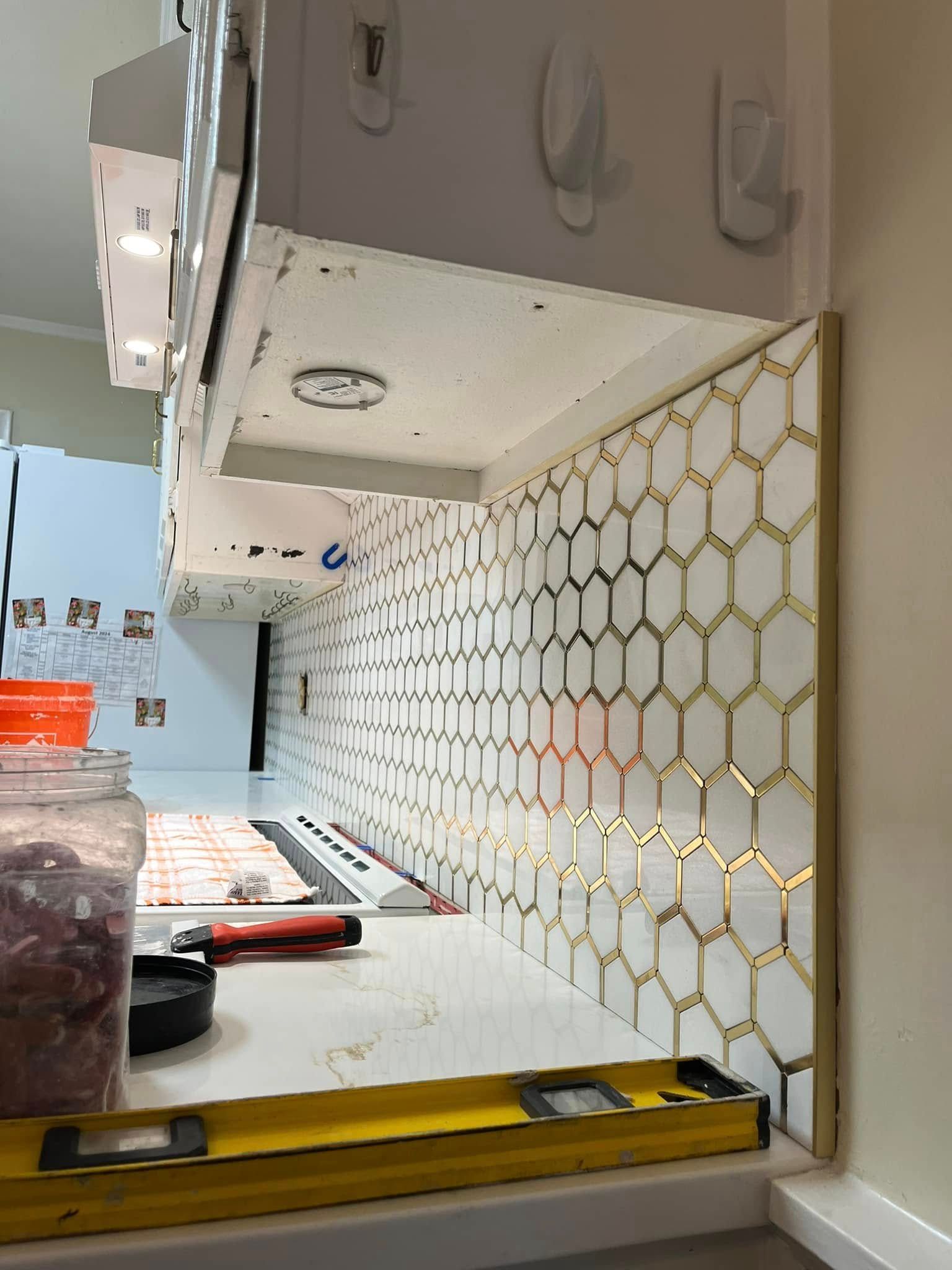 Installing white hexagon tiles with gold trim for a kitchen backsplash; level in place.