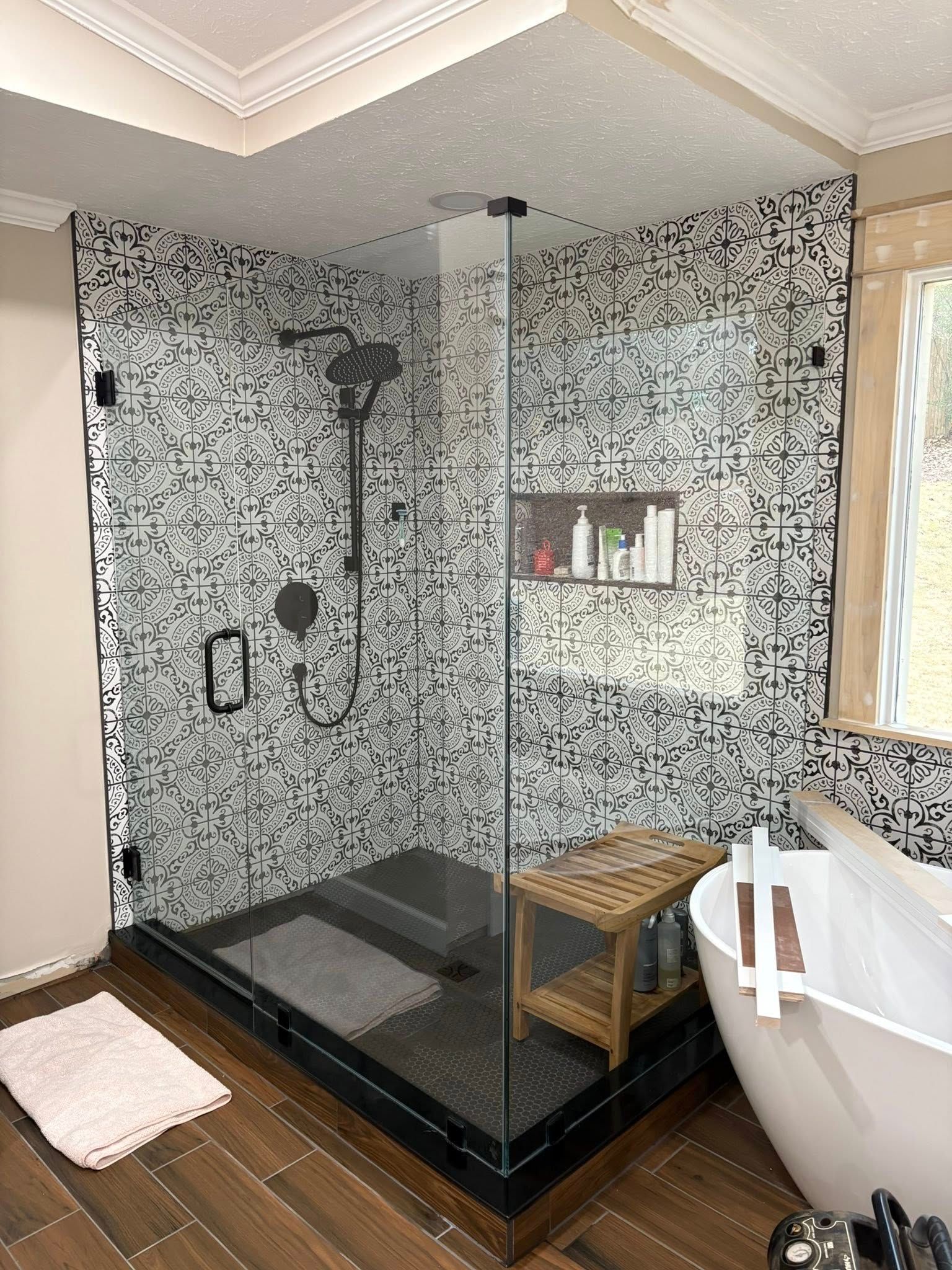 Modern bathroom with black and white tiled shower, glass doors, and a wooden bench.