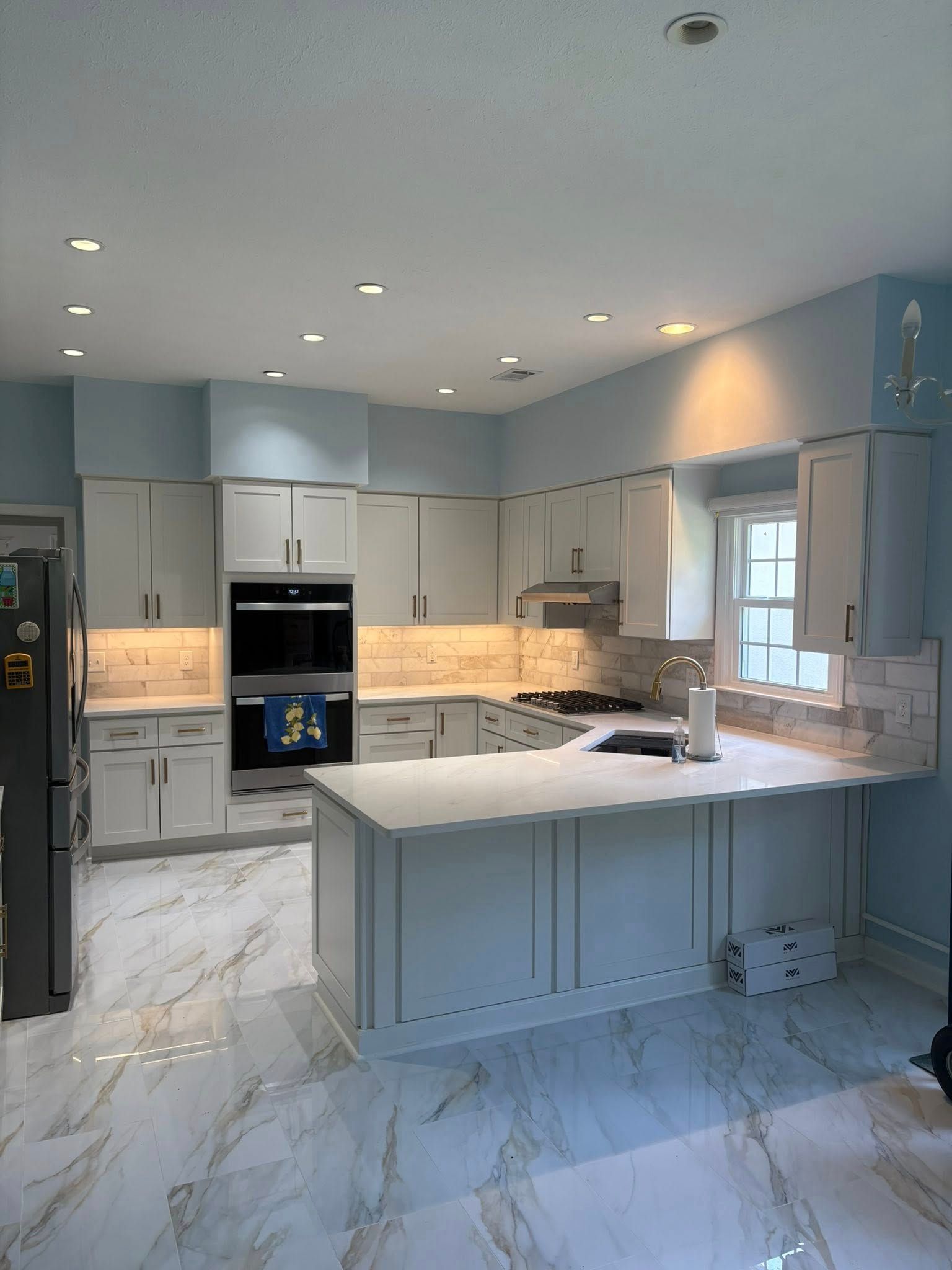 Modern kitchen with light blue walls, white cabinets, marble floors, and an island.