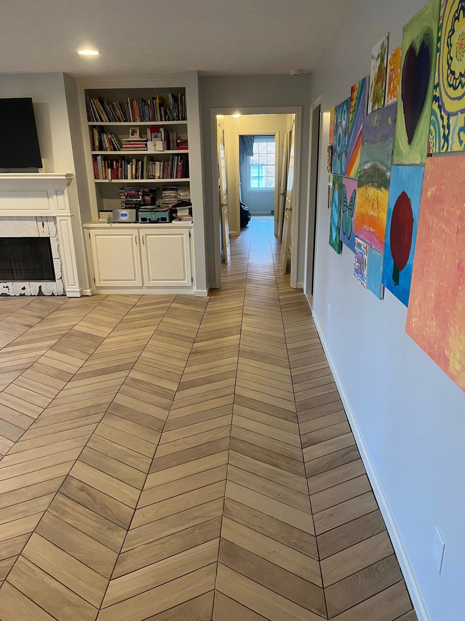 Living room with light wood herringbone floors, bookcase, art on wall, and a hallway.