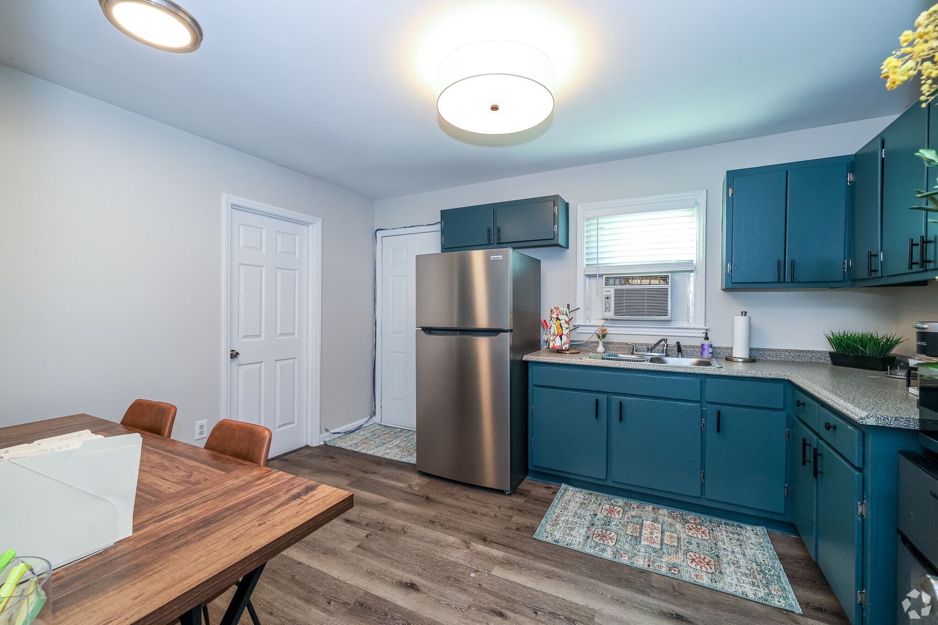 Kitchen with teal cabinets, stainless steel refrigerator, and wooden table.