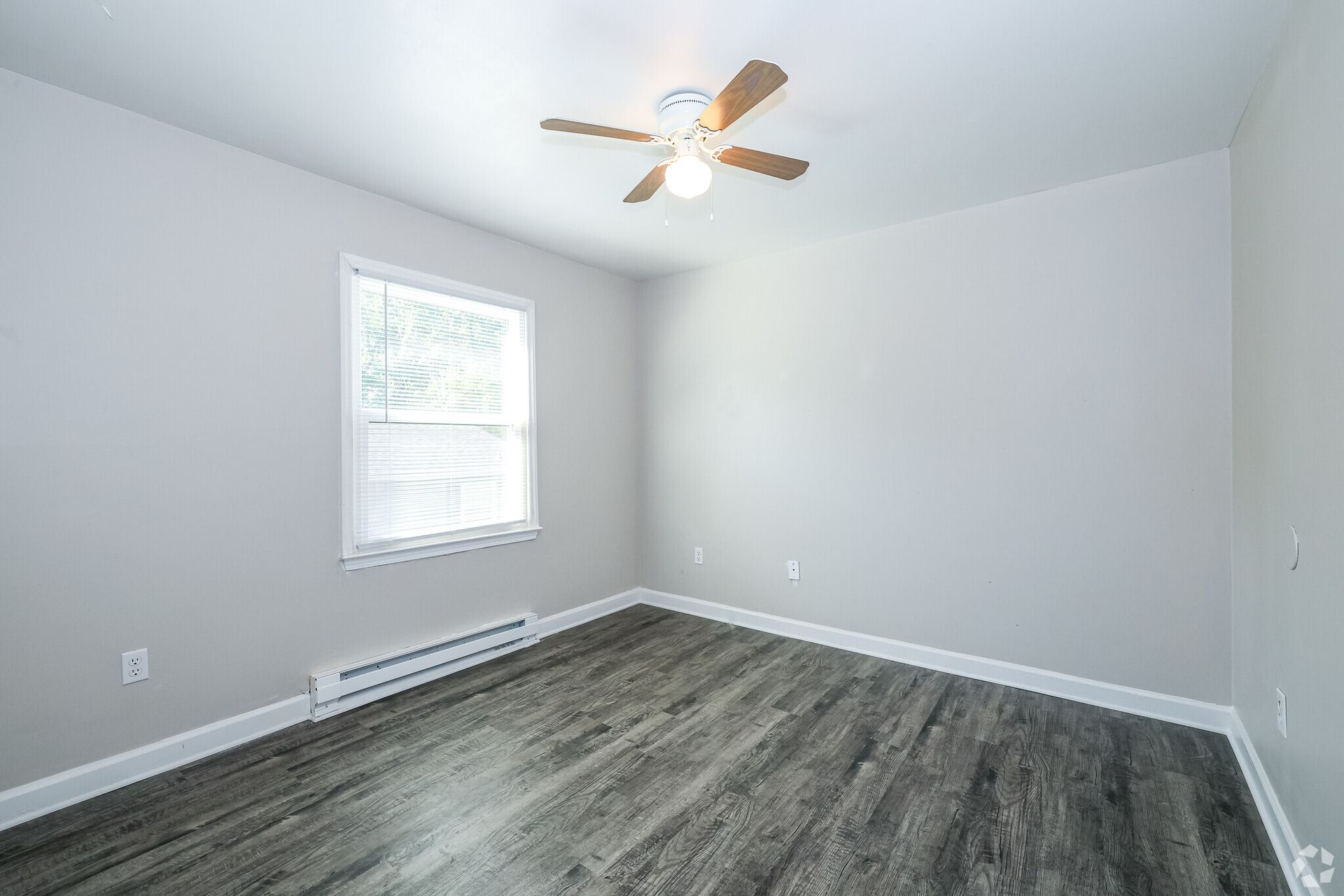 Empty bedroom with gray walls, wood-look floor, window, and ceiling fan.