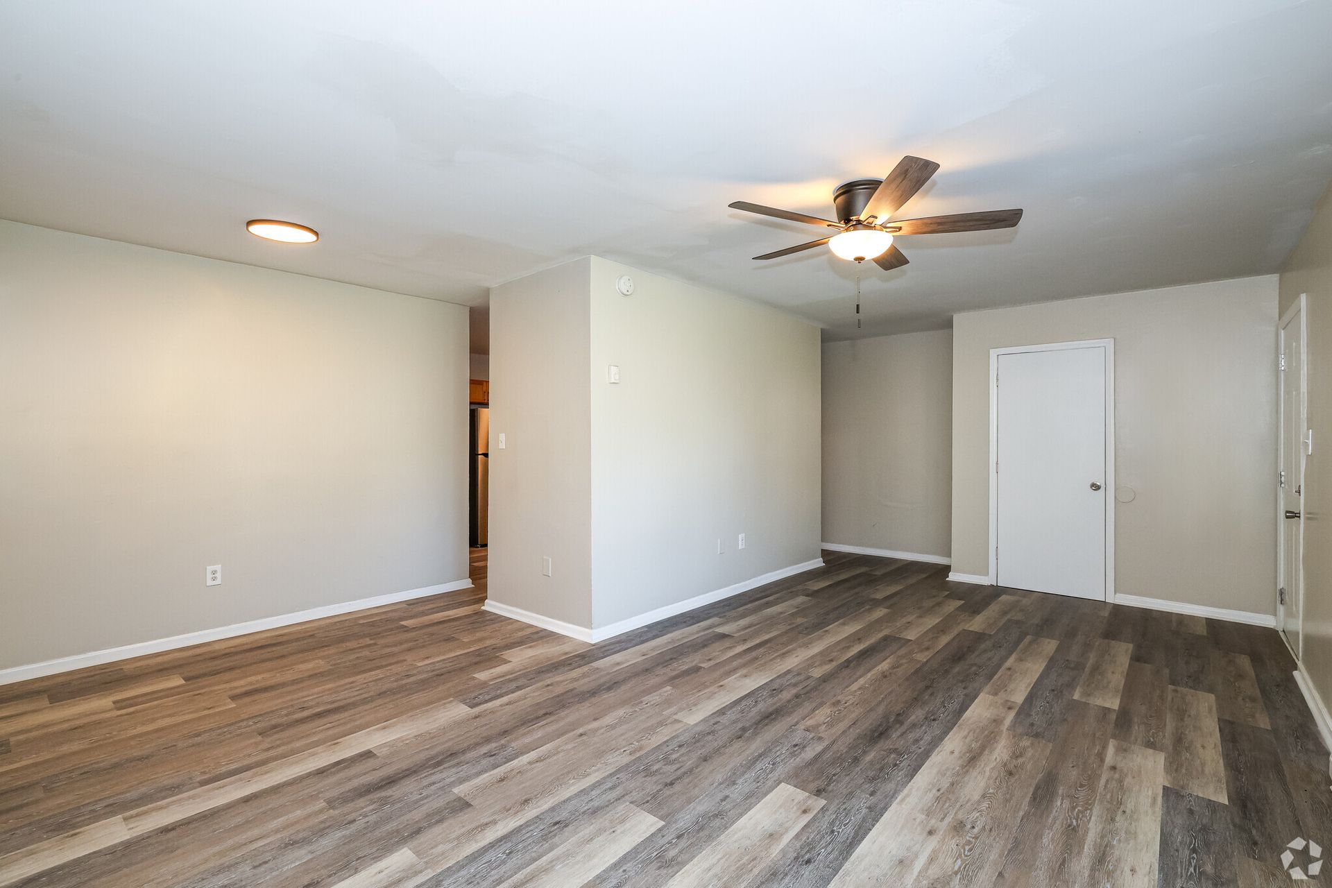 Empty living room with light grey walls, wood-look flooring, ceiling fan, and white door.