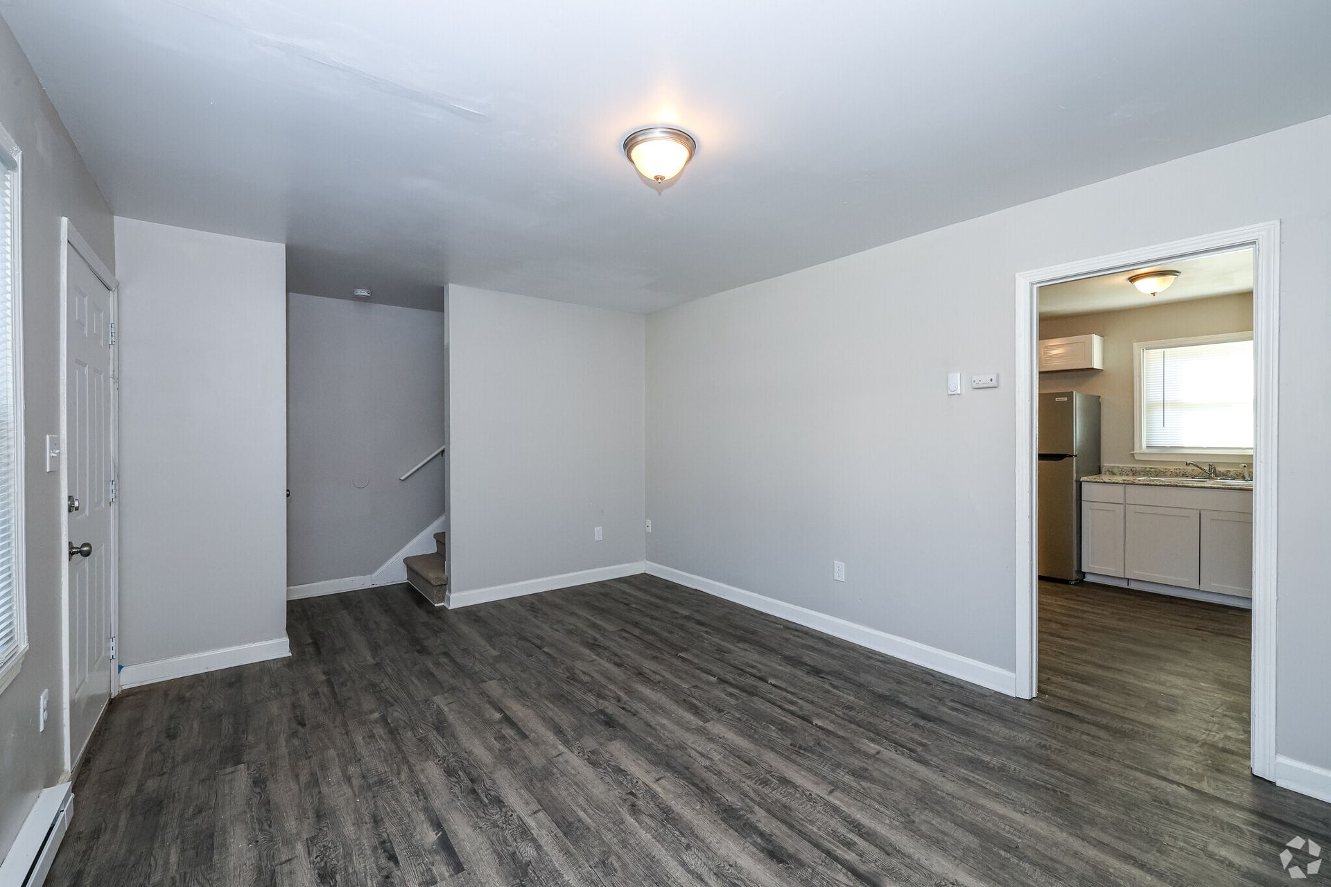 Empty living room with gray walls, wood-look flooring, and a doorway to a kitchen.