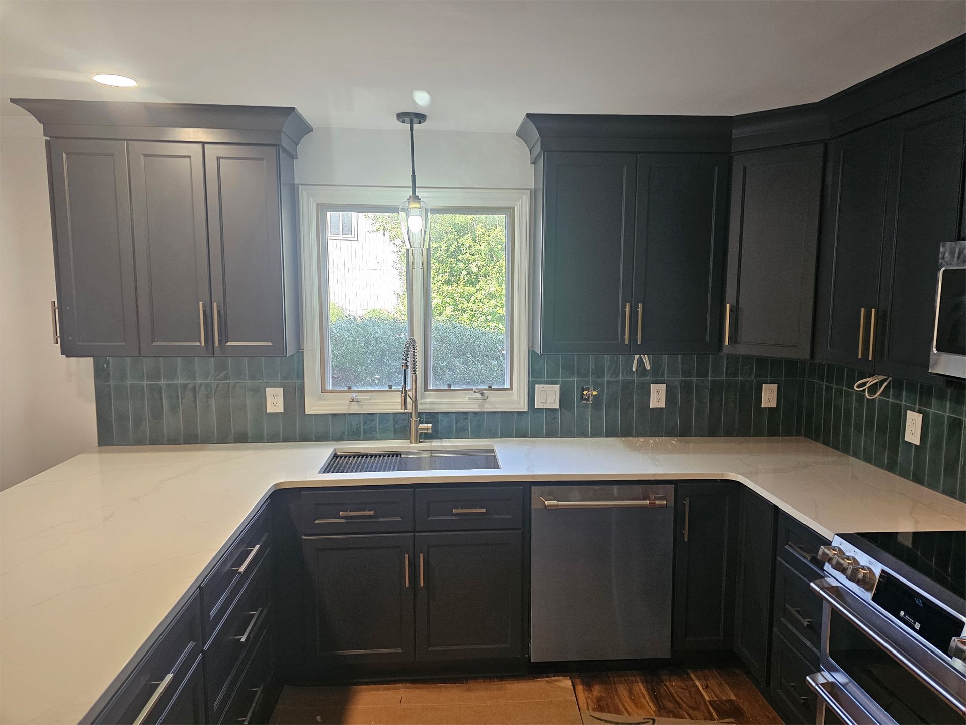 A kitchen with dark navy cabinets, white countertops, and a green tiled backsplash, featuring a sink and a dishwasher.