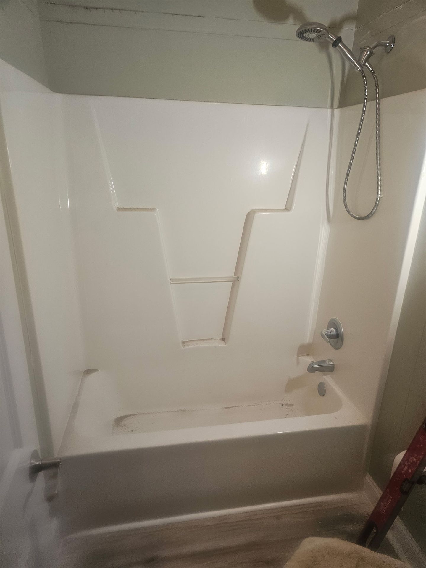 White bathtub and shower surround with a handheld shower head mounted on a light-colored wall.
