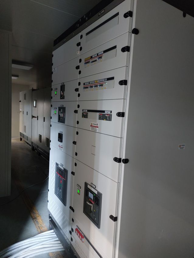 Pannelli di controllo elettrici industriali bianchi lungo un corridoio poco illuminato, con etichette di avvertimento e interruttori.