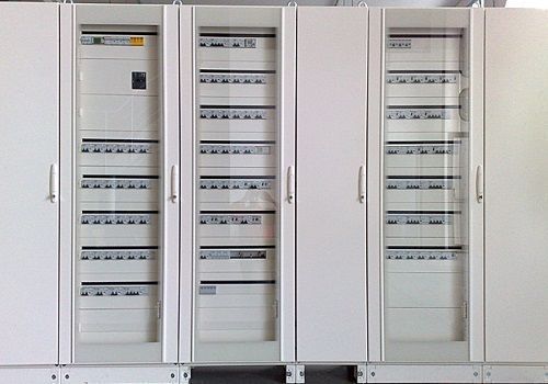 Armadi di controllo elettrico bianchi con ante in vetro e file di interruttori automatici in un locale di servizio.