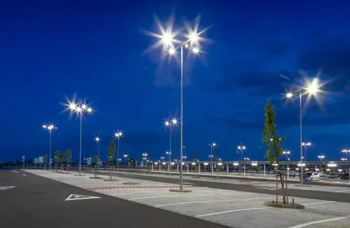 Parcheggio vuoto al crepuscolo, illuminato dai lampioni sotto un cielo blu intenso.