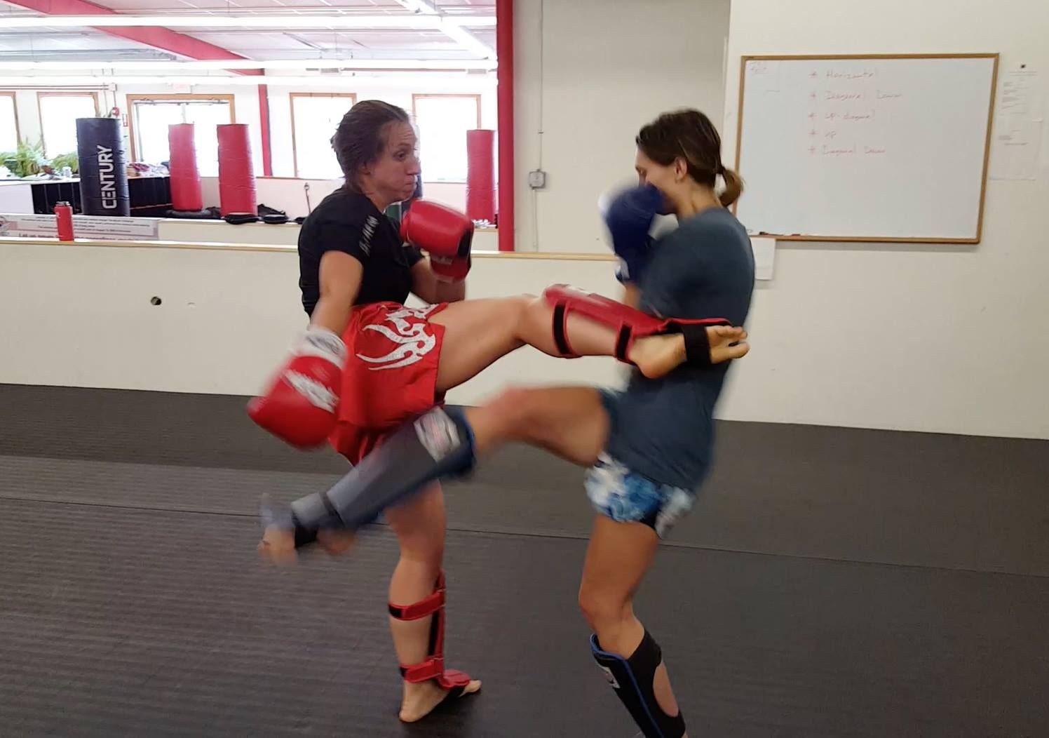two women are kickboxing in a gym with a white board in the background