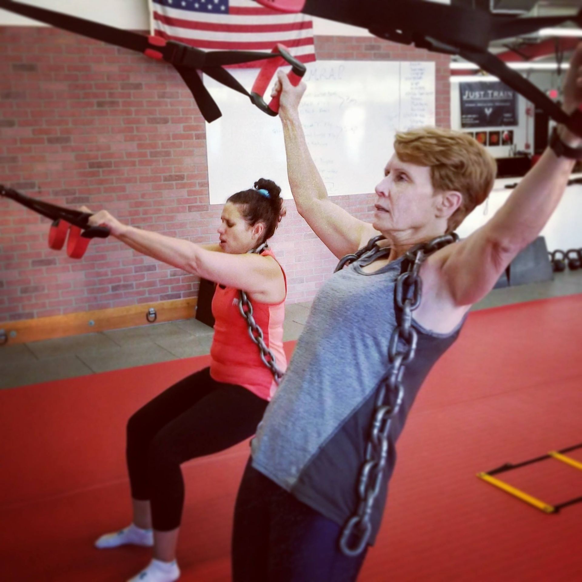 two women are doing exercises in a gym with an american flag in the background