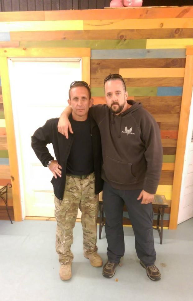 two men are standing next to each other in a room with pictures on the wall .