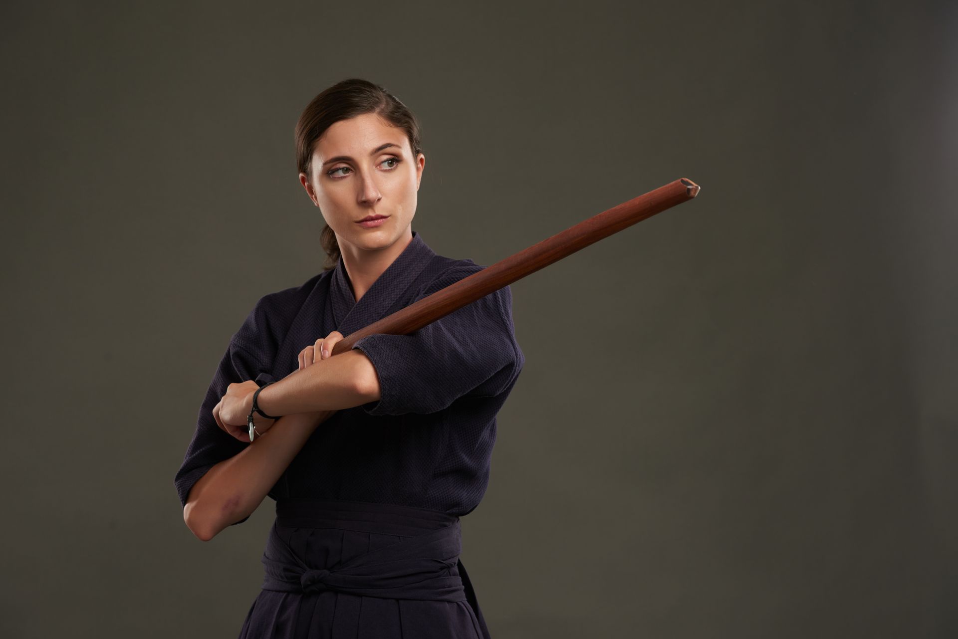 a woman in a karate uniform is holding a wooden stick .