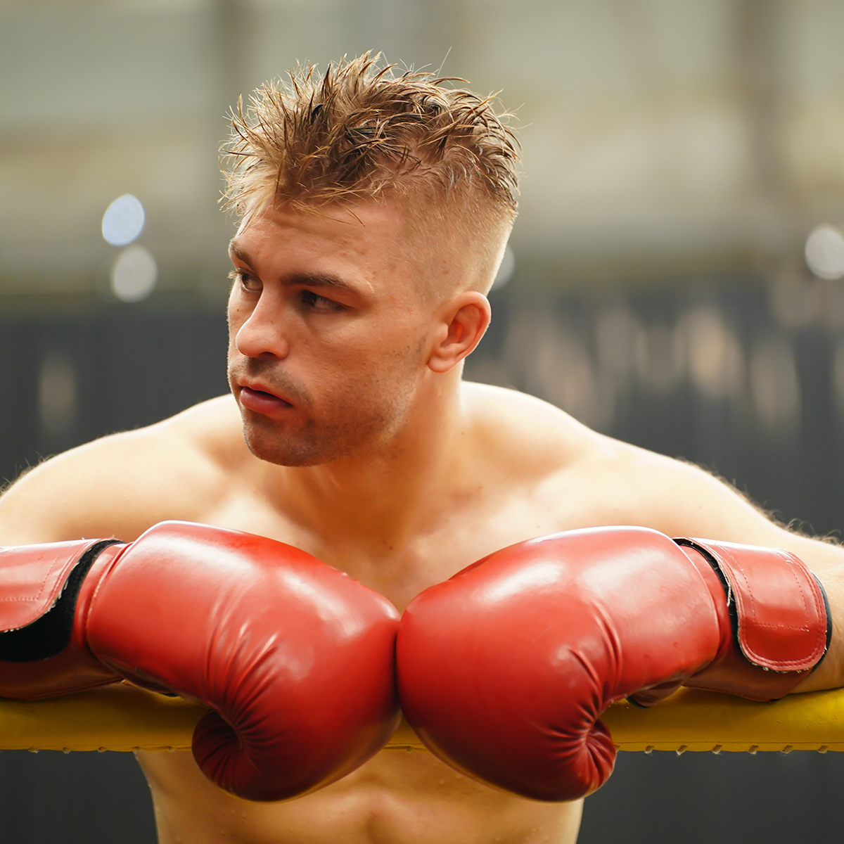 a shirtless man wearing red boxing gloves is standing in a boxing ring .